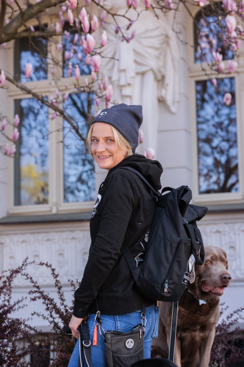 HeartcoredogsBerlin - Hundetraining - Magdalena lächelt inmitten von drei verschiedenfarbigen Hunden in einer verschneiten Umgebung